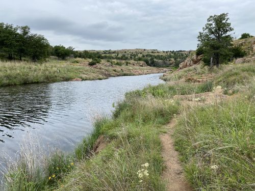 A serene river winding through grassy banks and hills under a cloudy sky.