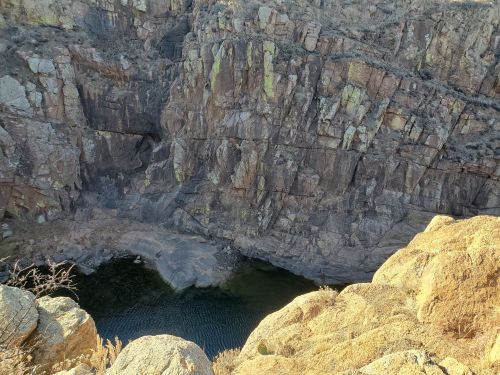 A rocky canyon with steep cliffs surrounding a small, calm body of water at the bottom.
