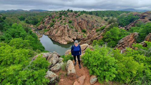 A person stands on a rocky outcrop surrounded by lush greenery and a winding river in a scenic landscape.