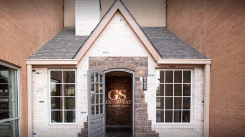 Entrance of a building featuring a stone archway, large windows, and a sign that reads "GS Sweat."