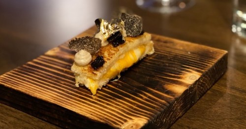 A gourmet dish featuring a layered pastry with cheese, topped with truffle slices and garnished on a wooden board.