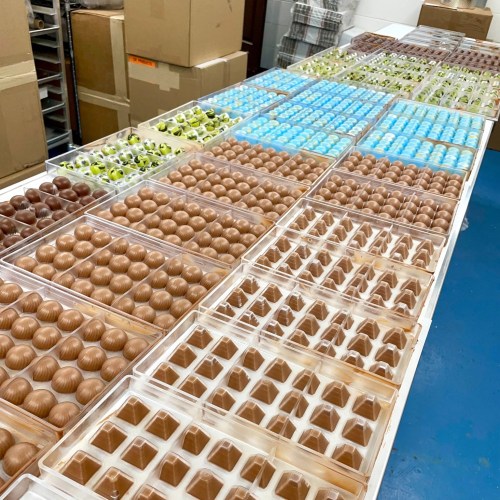 A table filled with neatly arranged trays of assorted chocolates in various colors and shapes.