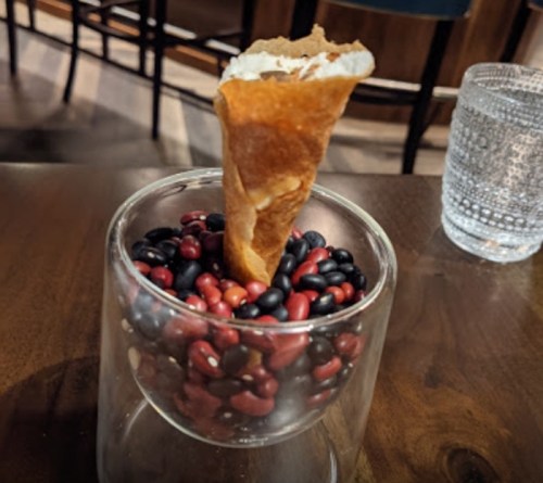 A glass filled with mixed beans and a small cone resting on top, placed on a wooden table.