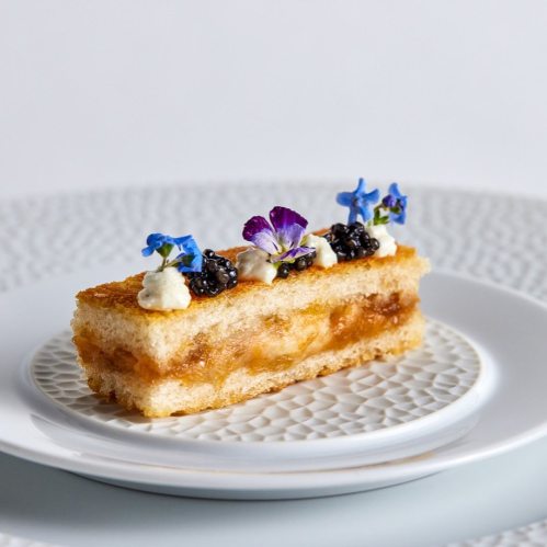 A layered dessert with fruit filling, topped with cream, caviar, and edible flowers, served on a decorative plate.