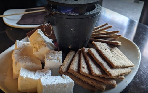 A plate with graham crackers, marshmallows, and a small pot for melting chocolate.