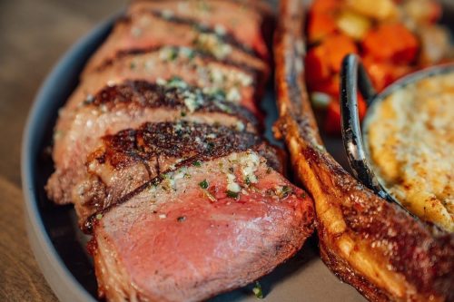 A plate featuring sliced roast beef with herbs, accompanied by roasted vegetables and a side dish.