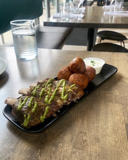 A plate with grilled meat topped with green sauce, accompanied by fried balls and a small bowl of dipping sauce.
