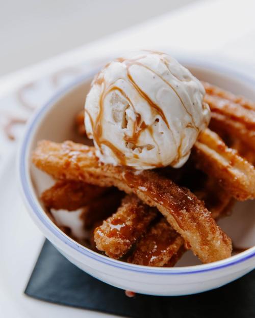 A bowl of churros topped with a scoop of vanilla ice cream and drizzled with caramel sauce.