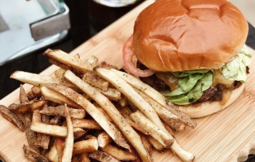 A juicy burger with lettuce, tomato, and cheese, served with a side of crispy fries on a wooden board.