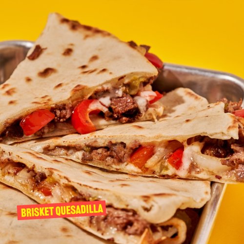 A close-up of a brisket quesadilla, filled with beef, peppers, and cheese, served on a metal tray.