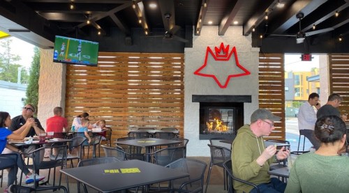 Interior of a restaurant with a fireplace, seating area, and a TV showing a game, featuring a red logo on the wall.