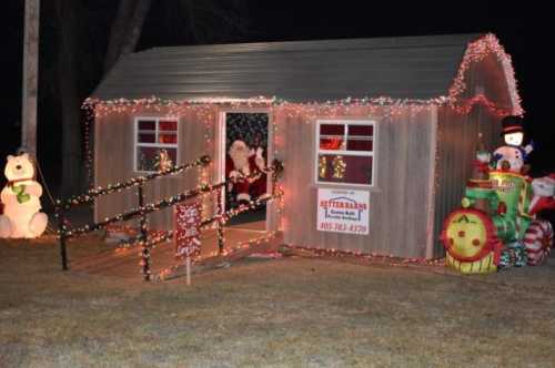 A festive shed decorated with Christmas lights, featuring Santa, a snowman, and holiday decorations.