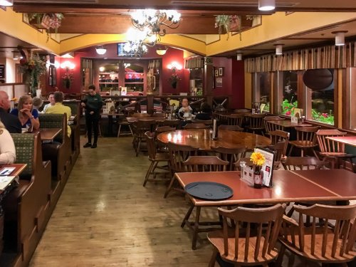 A cozy restaurant interior with wooden tables, chairs, and patrons enjoying their meals in a warm atmosphere.