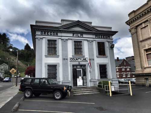 Historic building with "Oregon Film Museum" sign, featuring a gray facade and a parked black SUV in front.