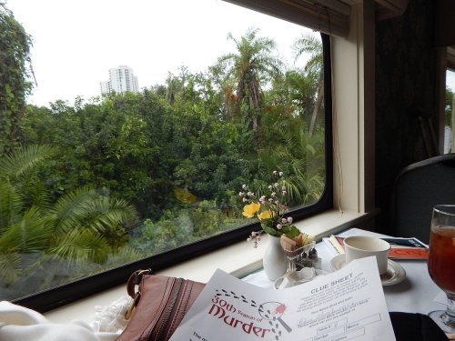 A table with a menu, a cup, and a small vase, overlooking a lush green landscape through a large window.