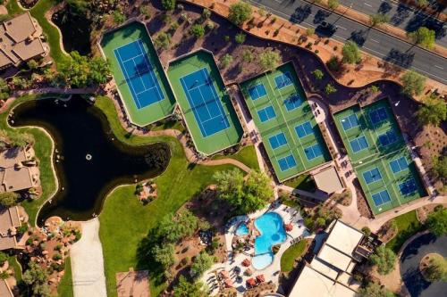 Aerial view of a resort featuring multiple tennis courts, a pool, and landscaped areas with a pond.