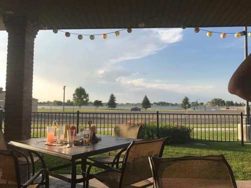View from a patio with a table set for dining, overlooking a grassy area and a road under a blue sky with clouds.