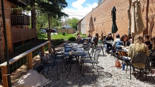 Outdoor dining area with tables and chairs, surrounded by greenery, where a group of people are enjoying a meal.