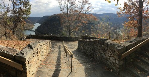 Scenic view of a river winding through autumn-colored hills, with stone steps leading down from a viewpoint.