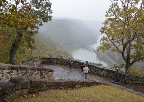 A misty landscape view from a stone overlook, with a river and train bridge in the distance, surrounded by trees.