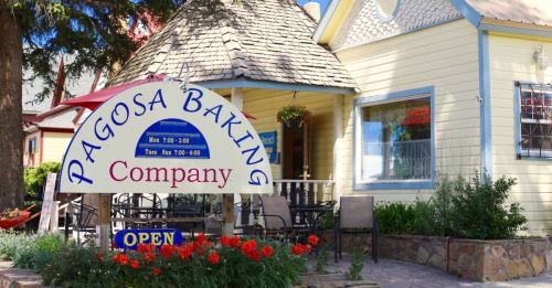 A charming yellow building with a sign for "Pagosa Baking Company" and red flowers in front, indicating it's open.