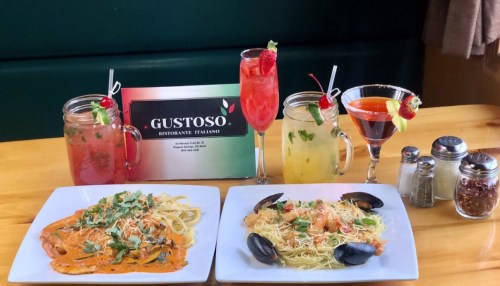 A table with two pasta dishes, colorful cocktails, and a restaurant sign, showcasing a vibrant Italian dining experience.