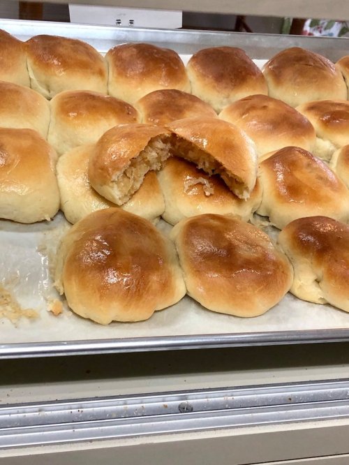 Freshly baked golden-brown rolls on a tray, with one roll cut open to reveal a fluffy interior.