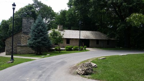 A stone building surrounded by trees, with a winding road leading up to it and a grassy area in the foreground.