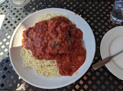 A plate of spaghetti topped with a rich tomato sauce and meatballs, served on a black table.