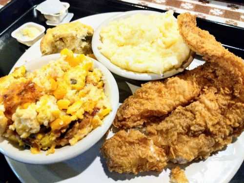 A plate featuring fried fish, creamy mashed potatoes, cornbread, and a corn casserole.