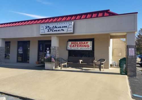 Exterior of Pelham Diner with a red roof, seating area, and a sign for holiday catering. Clear blue sky above.