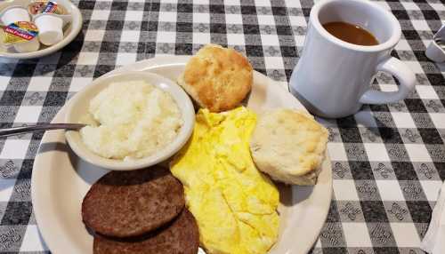 A plate with eggs, sausage, grits, a biscuit, and a cup of coffee on a checkered tablecloth.