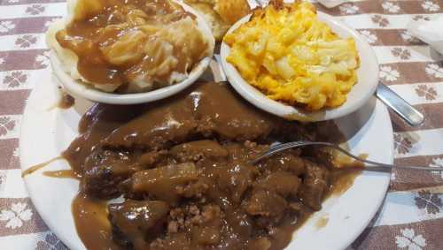 A plate of meatloaf with gravy, mashed potatoes, and macaroni and cheese, served on a checkered tablecloth.