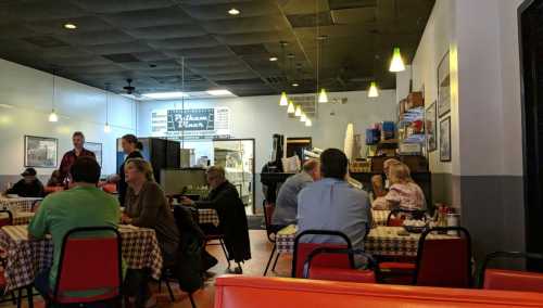 A cozy diner interior with checkered tables, patrons dining, and a menu board in the background. Warm lighting and casual atmosphere.