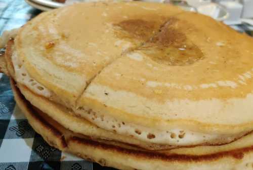 A stack of golden-brown pancakes with a small pat of butter melting on top, placed on a checkered tablecloth.