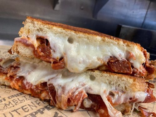 A close-up of a grilled cheese sandwich filled with pepperoni and melted cheese, served on parchment paper.