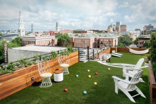 Rooftop terrace with green grass, chairs, a hammock, and a view of a city skyline and church steeples.