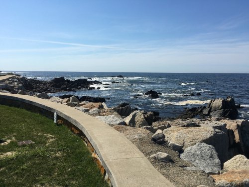 A coastal view featuring rocky shores and gentle waves under a clear blue sky.