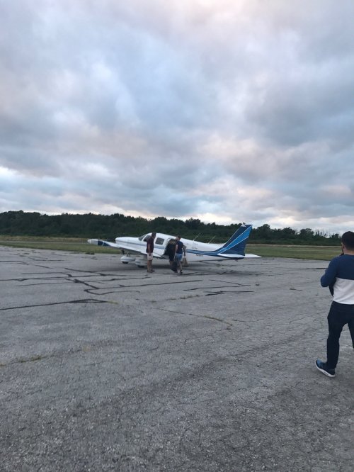 Two people walk towards a small airplane on an airstrip under a cloudy sky.