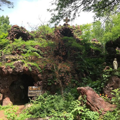 Entrance to Wonder Cave, surrounded by lush greenery and colorful flowers, with a statue nearby.