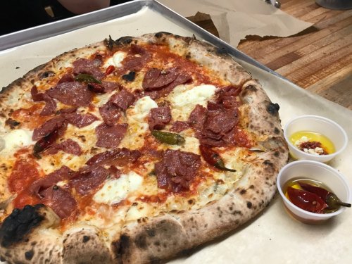 A freshly baked pizza topped with pepperoni and mozzarella, served with two small cups of dipping sauces.