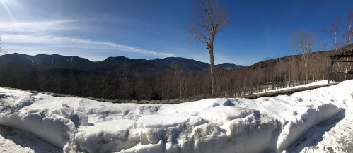 Panoramic view of snow-covered landscape with mountains and clear blue sky in the background.
