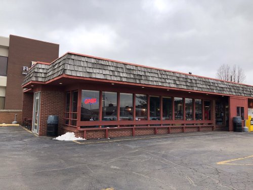 A single-story restaurant with a shingled roof, large windows, and a neon "Open" sign, set against a cloudy sky.