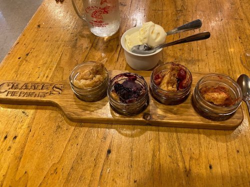 A wooden board with four small jars of pie fillings and a scoop of ice cream on the side, set on a rustic table.