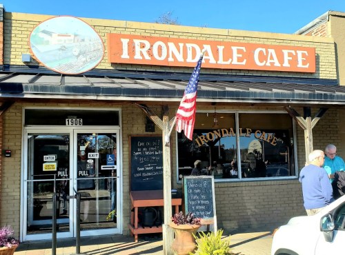 Exterior of Irondale Cafe with a sign, American flag, and people gathered outside on a sunny day.