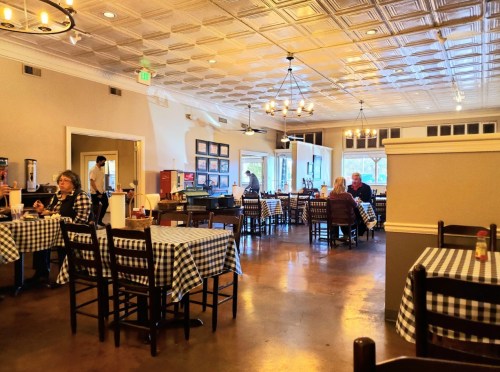 A cozy restaurant interior with checkered tablecloths, wooden chairs, and diners enjoying their meals.