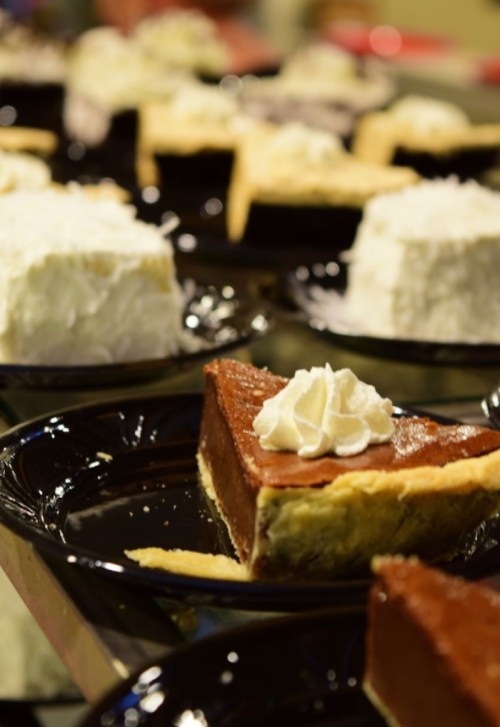 A variety of pies on black plates, featuring chocolate and cream pies with whipped cream toppings.