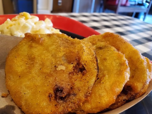 Three golden, crispy fried green tomatoes served with a side of creamy macaroni and cheese on a checkered tablecloth.