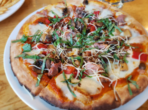 A delicious pizza topped with cheese, mushrooms, ham, tomatoes, and fresh basil on a wooden table.