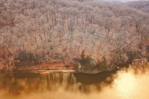 Aerial view of a serene river bordered by trees, reflecting golden hues in the water during autumn.
